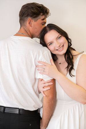 A smiling woman in a white dress embraces a man in a white t-shirt during a romantic couples portrait session.