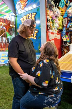 Young couple sharing a romantic moment at colorful carnival game booth at night.
