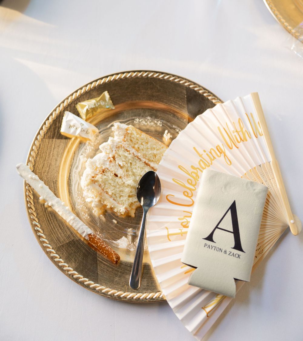 Gold metallic plate with leftover cake crumbs, a small spoon, monogrammed napkin and drink koozie at a wedding reception.