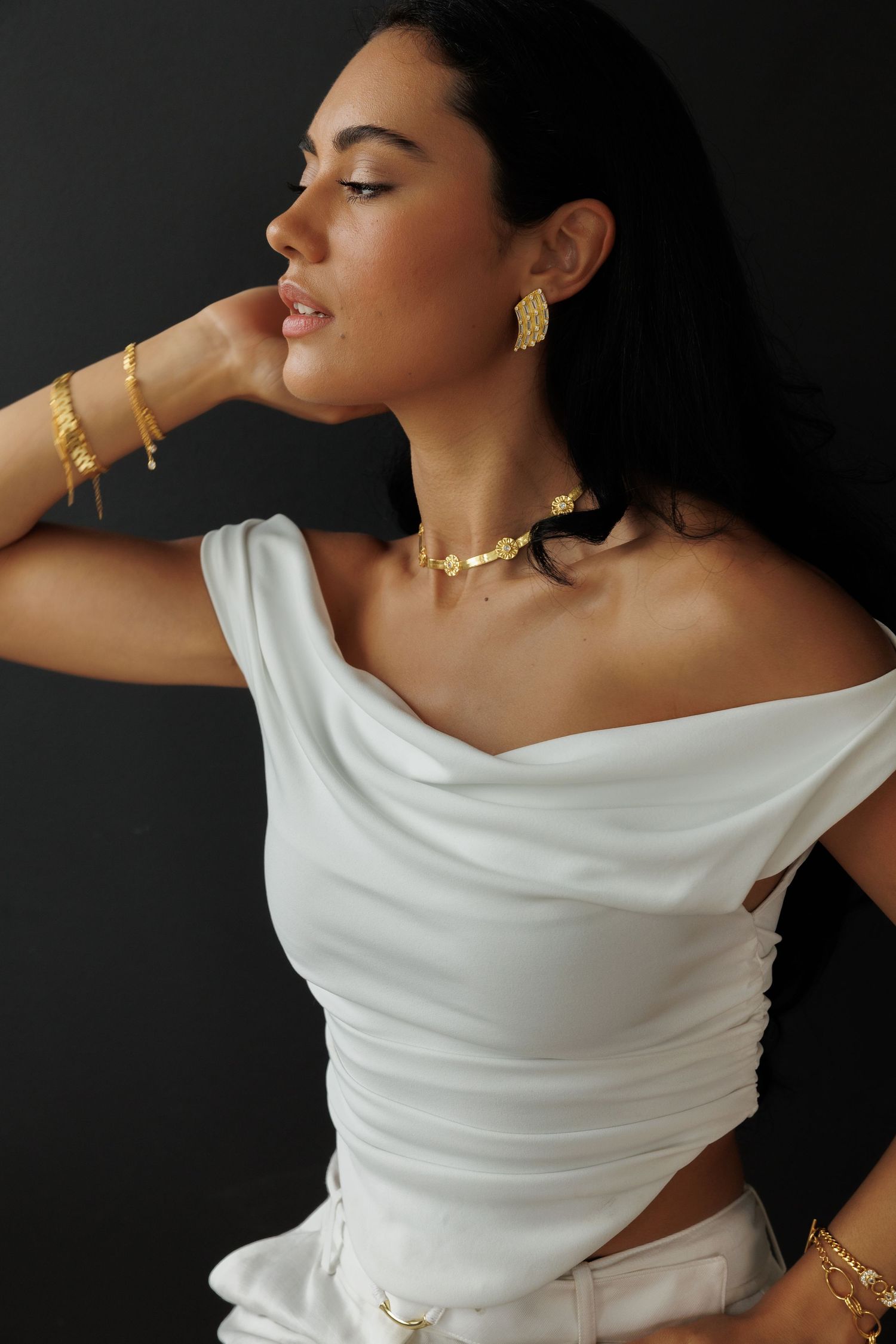 Houston jewelry brand photography by Gerry Myers Photo - woman in white dress wearing gold jewelry against dark background