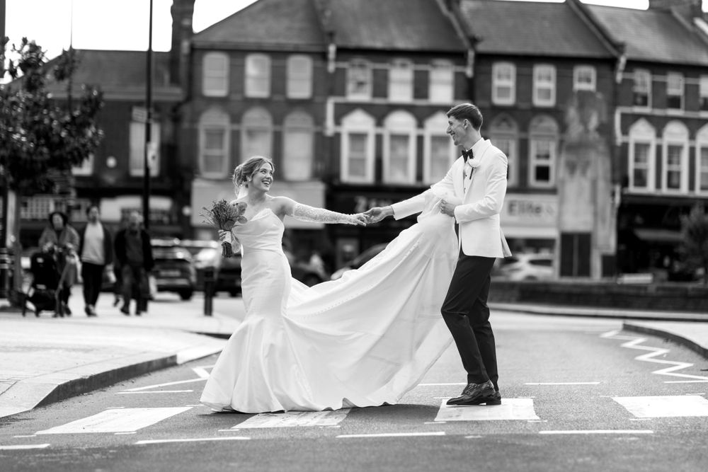 A couple in wedding attire dances together on a city street with their flowing white dress creating elegant movement.