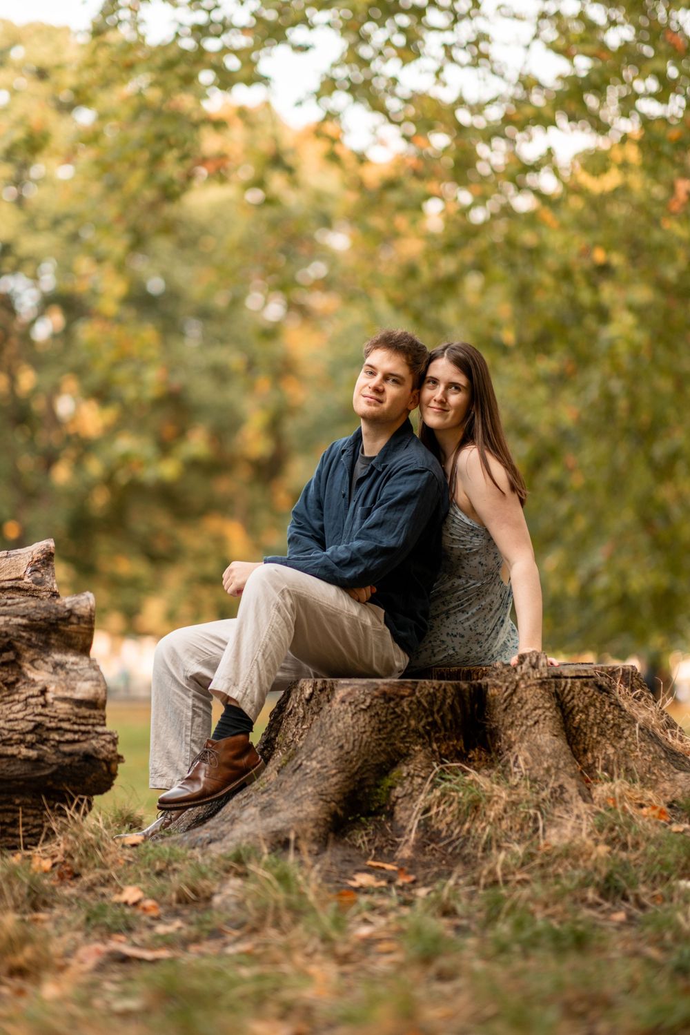 A couple sitting together on a tree stump surrounded by warm autumn colors.