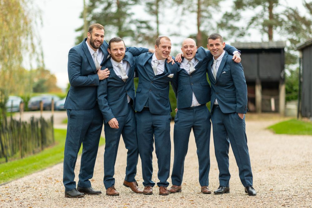 Groomsmen in matching navy suits pose casually together on a gravel path.