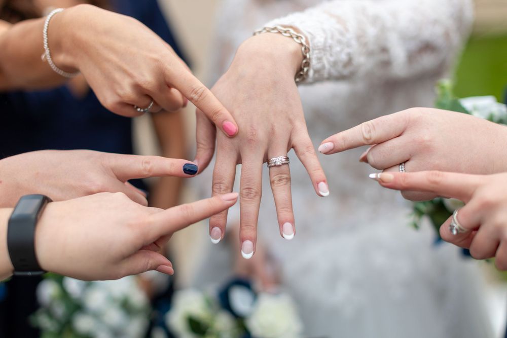 Multiple hands pointing at a new wedding ring on display.