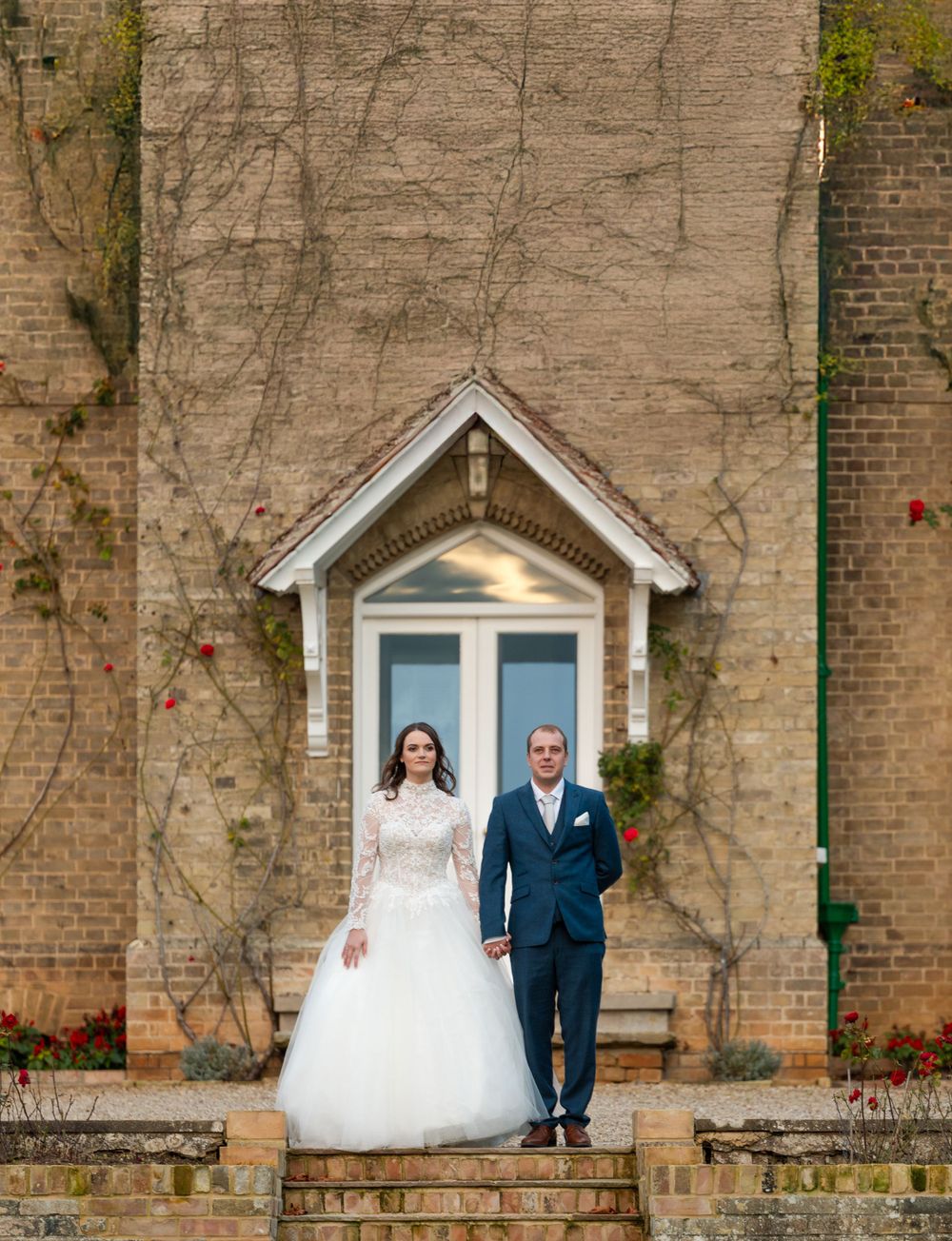 Wedding couple poses in front of brick building with white architectural doorway detail.