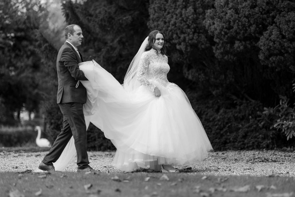Black and white photo of a flowing wedding dress being lifted while walking outdoors.