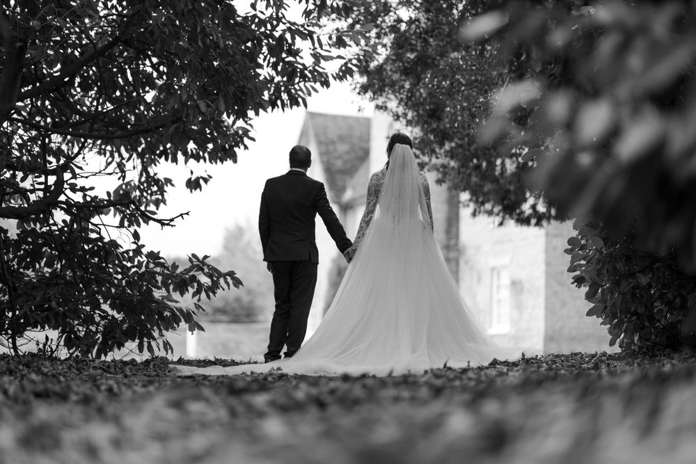 Silhouetted couple in wedding attire standing together under tree branches.