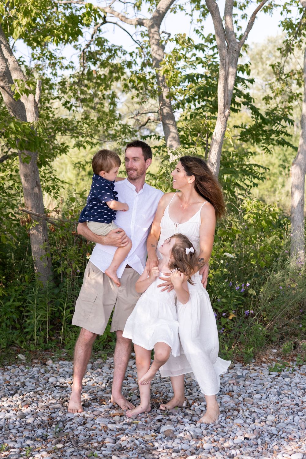 Family in white outfits sitting together on rocky beach while enjoying a casual outdoor photo session.