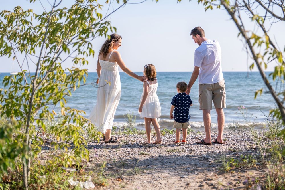 Family enjoying a sunny day collecting seashells together on a rocky beach by the ocean.Quinte West