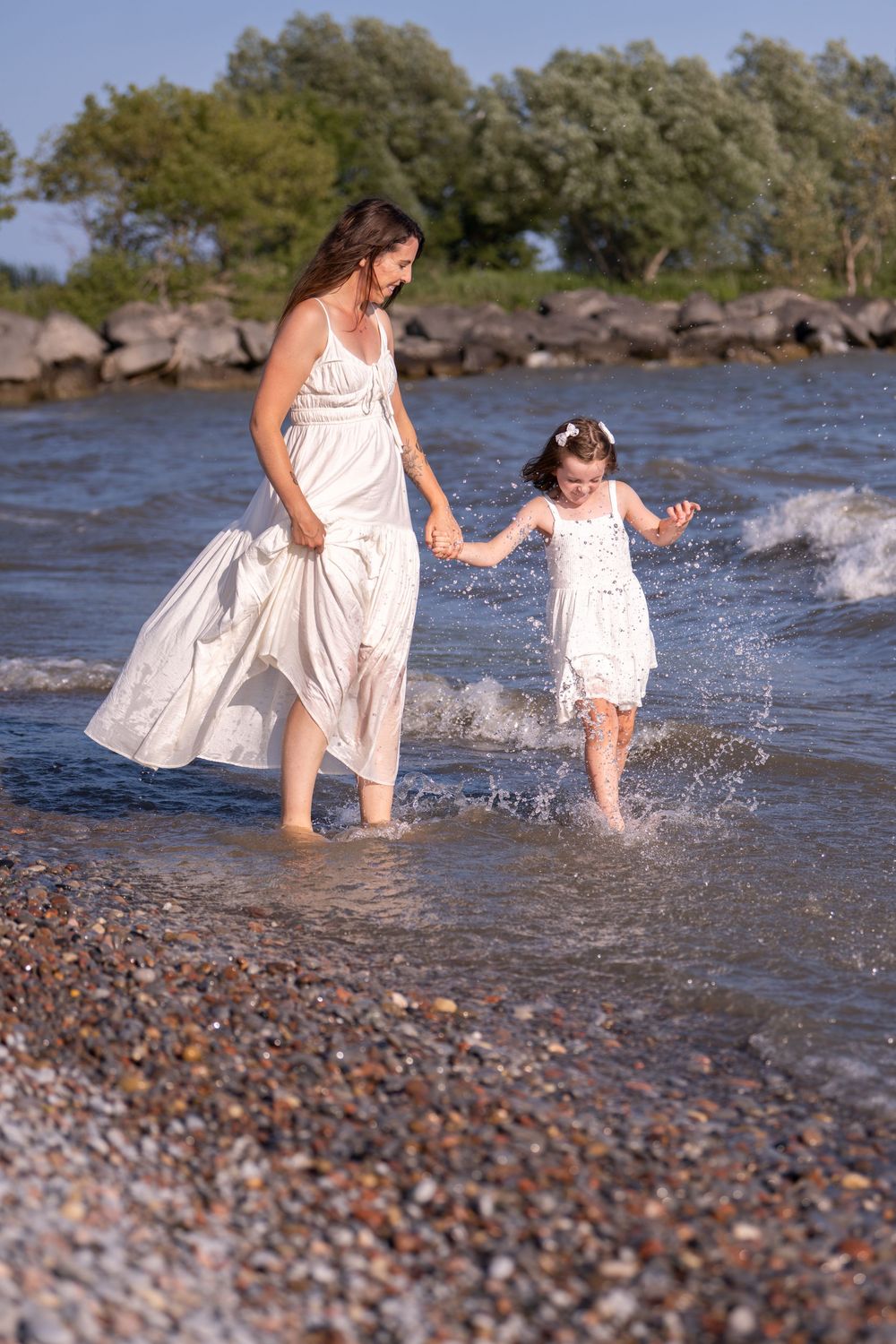 Two people in white dresses splash and play together at the rocky beach shoreline on a sunny day. Quinte West