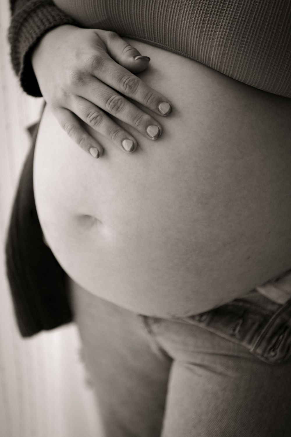 A black and white artistic photo of a pregnant belly with a gentle hand resting on top. Picton