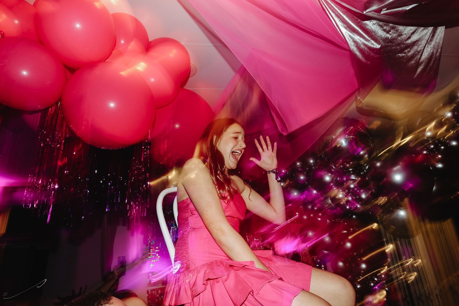 Excited young woman in pink dress celebrating at a vibrant pink balloon party.