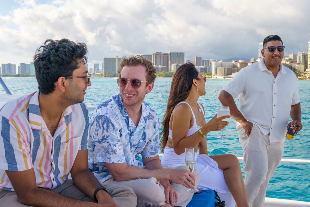 Yacht party guests enjoying drinks and conversation on deck with coastal skyline visible.