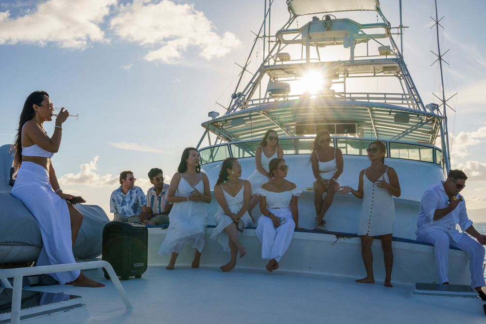 Party guests gathered on yacht deck during golden hour with cityscape in background.