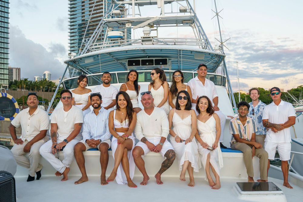 Group photo on luxury yacht deck with urban skyline visible in background.