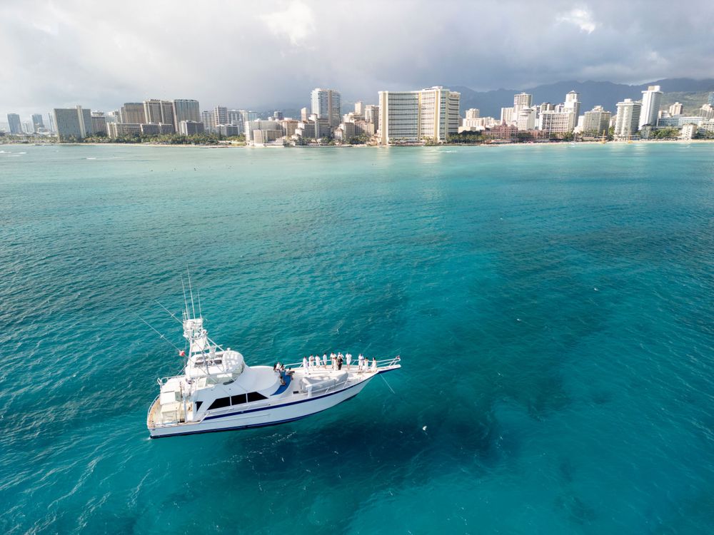 Aerial view of luxury yacht cruising in turquoise Hawaiian waters near Waikiki Beach.