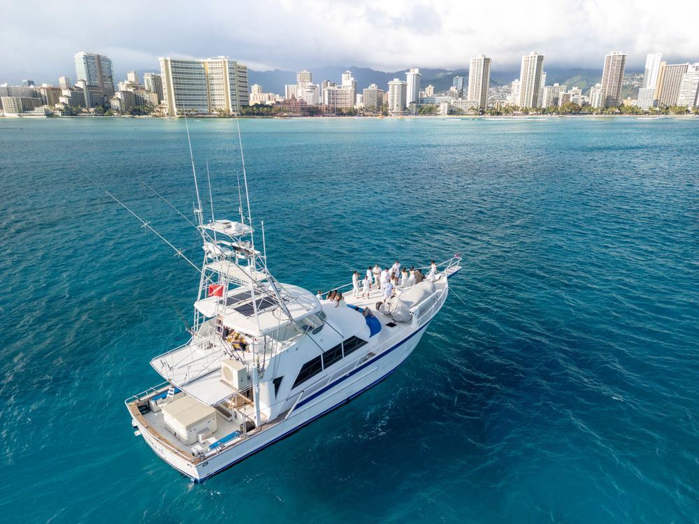 Drone shot of white yacht sailing in crystal clear blue ocean waters near coastal city.