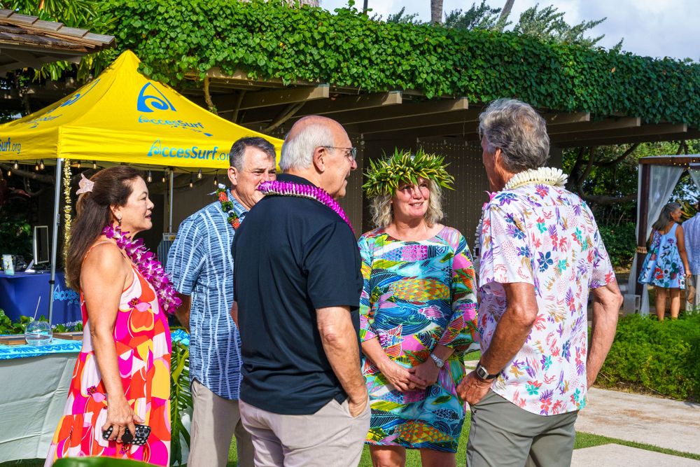 Colorfully dressed guests enjoying an outdoor tropical celebration under a yellow tent.
