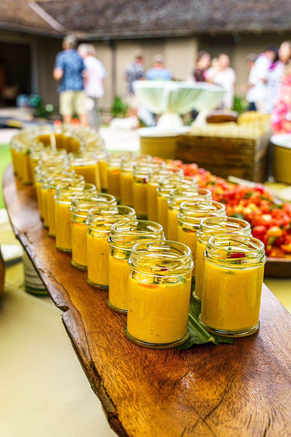 Rows of yellow smoothies in glass jars lined up on a rustic wooden table.