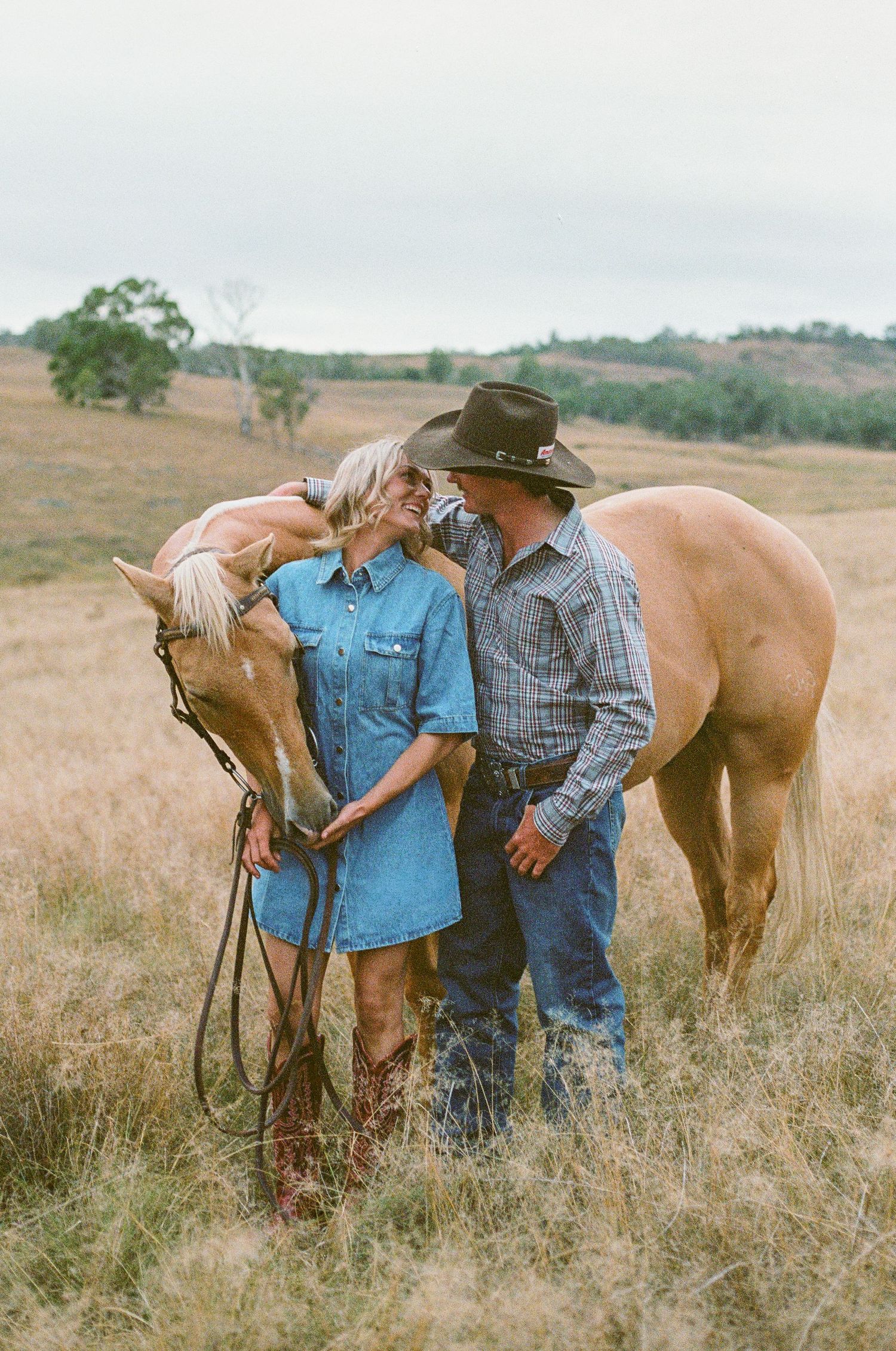 country couple looking into eachothers eyes while holding horse during western engagement photoshoot