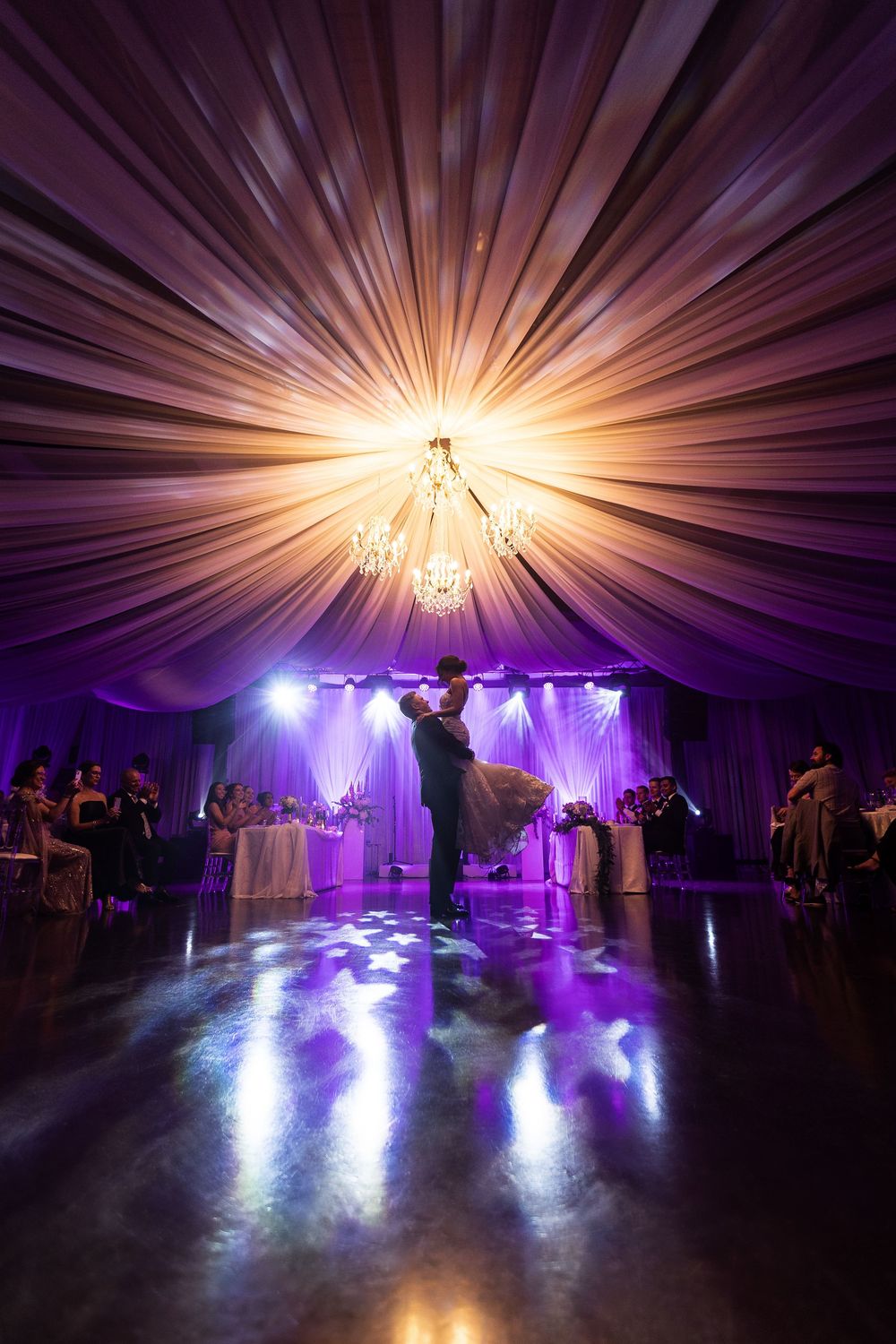 As a wedding couple dances, in front of dramatic purple and amber lighting, creating a stunning visual effect.  aKaiserPhoto.