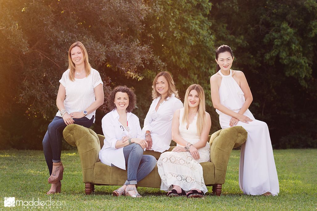 5 adult women friends wearing white sitting on green couch in a field