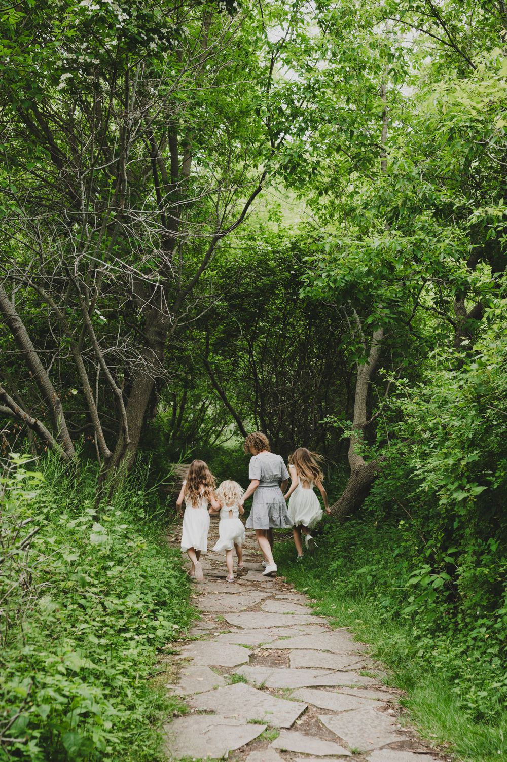 A group in white dresses walks along a stone path through lush green foliage.