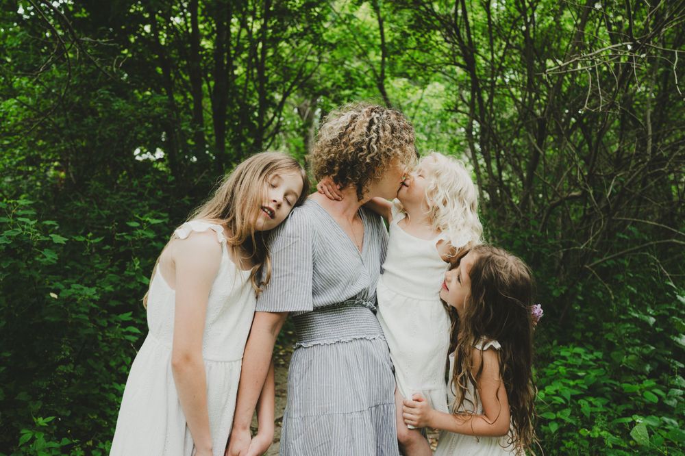 A tender moment shared between family members wearing light colored dresses in a wooded setting.