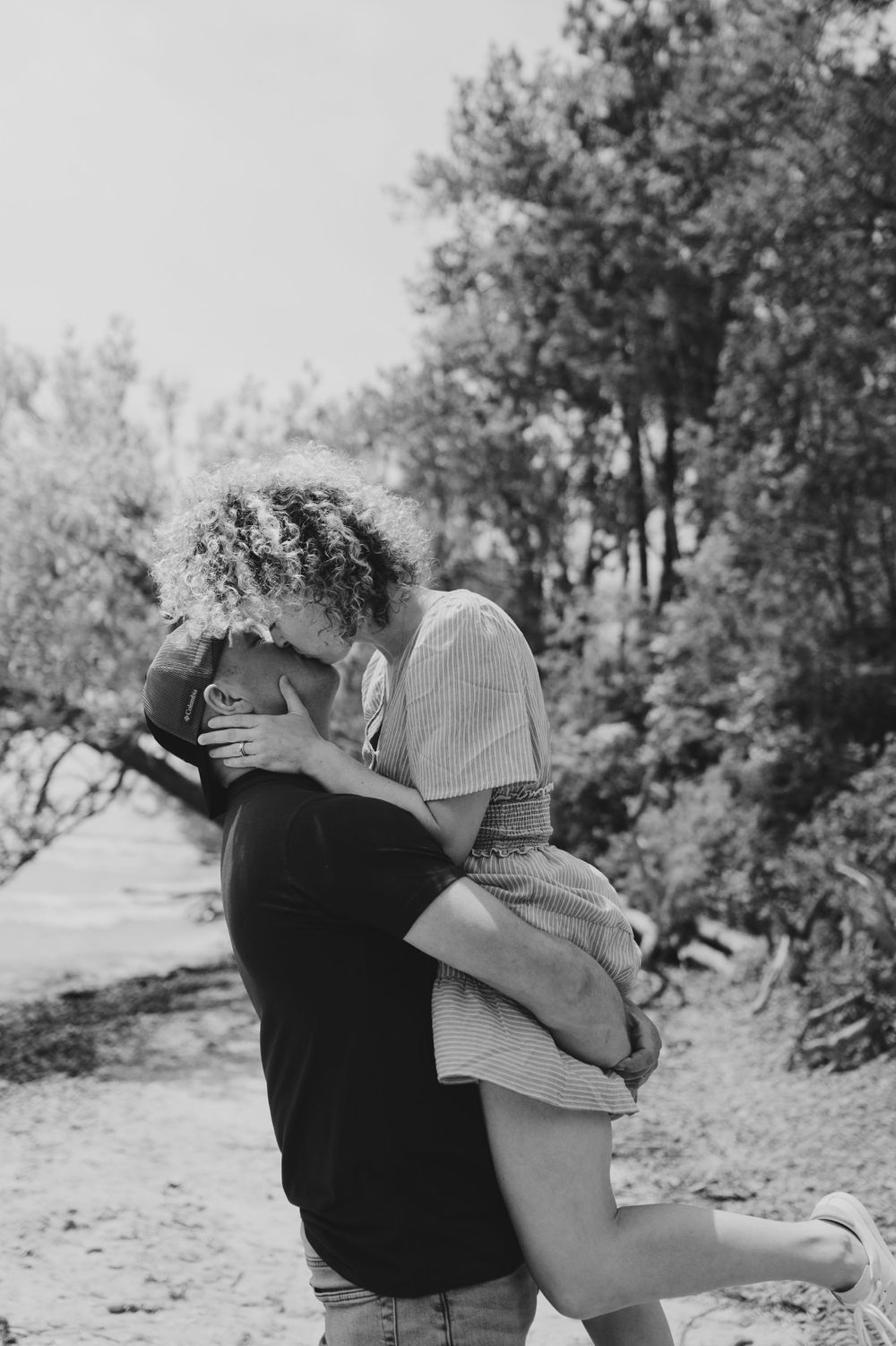 Black and white romantic moment captured between couple on a wooded path.