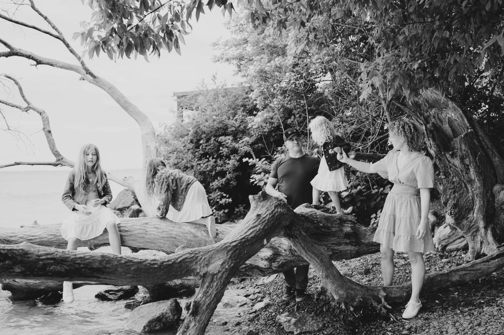 Vintage black and white photo of children playing on fallen tree branches near water.