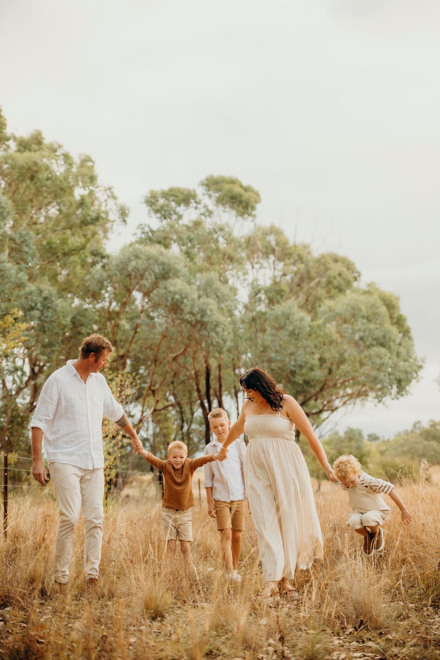 Happy family with three children walking through golden grass fields surrounded by eucalyptus trees.