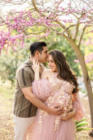 Couple embracing under pink cherry blossoms in spring garden setting.