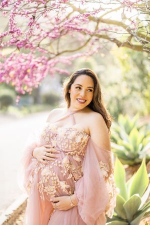 Romantic maternity photoshoot under blooming cherry blossom trees.
