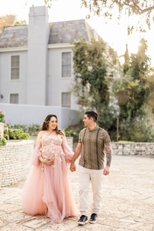 Couple in romantic engagement photos walking on stone path with woman wearing flowing pink tulle dress.