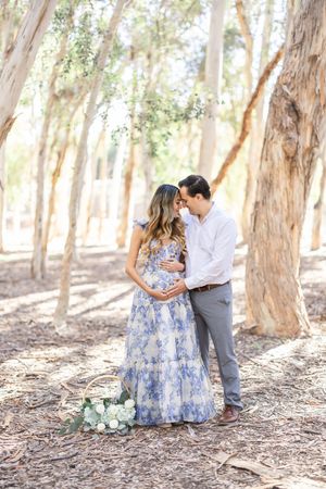 A couple shares an intimate moment in a eucalyptus grove while celebrating a maternity photoshoot.