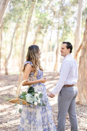 Couple in blue floral dress and white shirt holding hands in eucalyptus grove.
