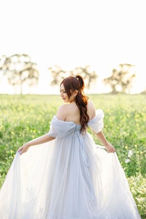 Elegant off-shoulder white gown flowing in the breeze against a meadow backdrop.