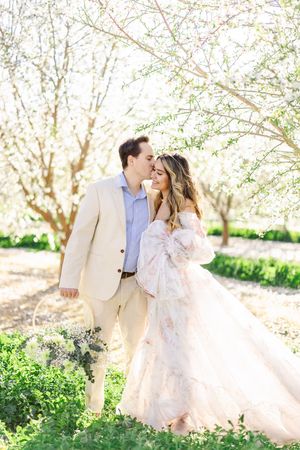 A romantic couple shares tender moments in a sun-drenched spring garden with blooming trees creating a dreamy atmosphere.