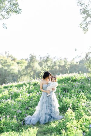 A couple in flowing dresses sits together in a lush green meadow on a sunny afternoon.