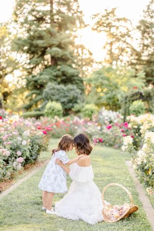 White-dressed figures sit among blooming rose garden paths at sunset.