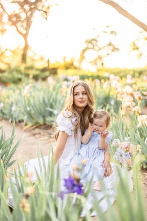 Mother and child share tender moment in spring garden filled with blooming iris flowers at sunset.