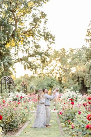 Family embraces in romantic rose garden setting during golden hour photography session.