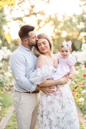 Family shares intimate moment together in blooming rose garden during sunset photoshoot.
