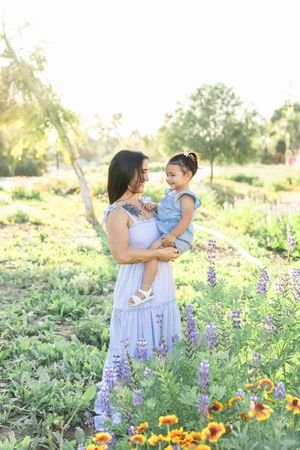 Mother and child standing among purple lupines and orange flowers in a garden.