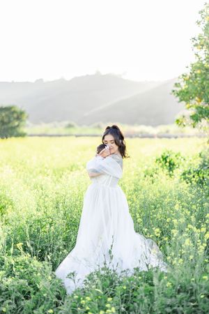 Ethereal portrait of a figure in a flowing white dress standing in a sunlit meadow of wildflowers.