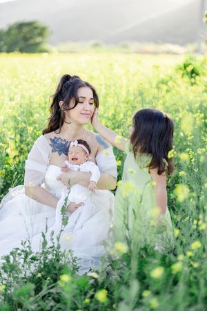 Family portrait in a golden meadow with a baby and flowing white dress against mountains.
