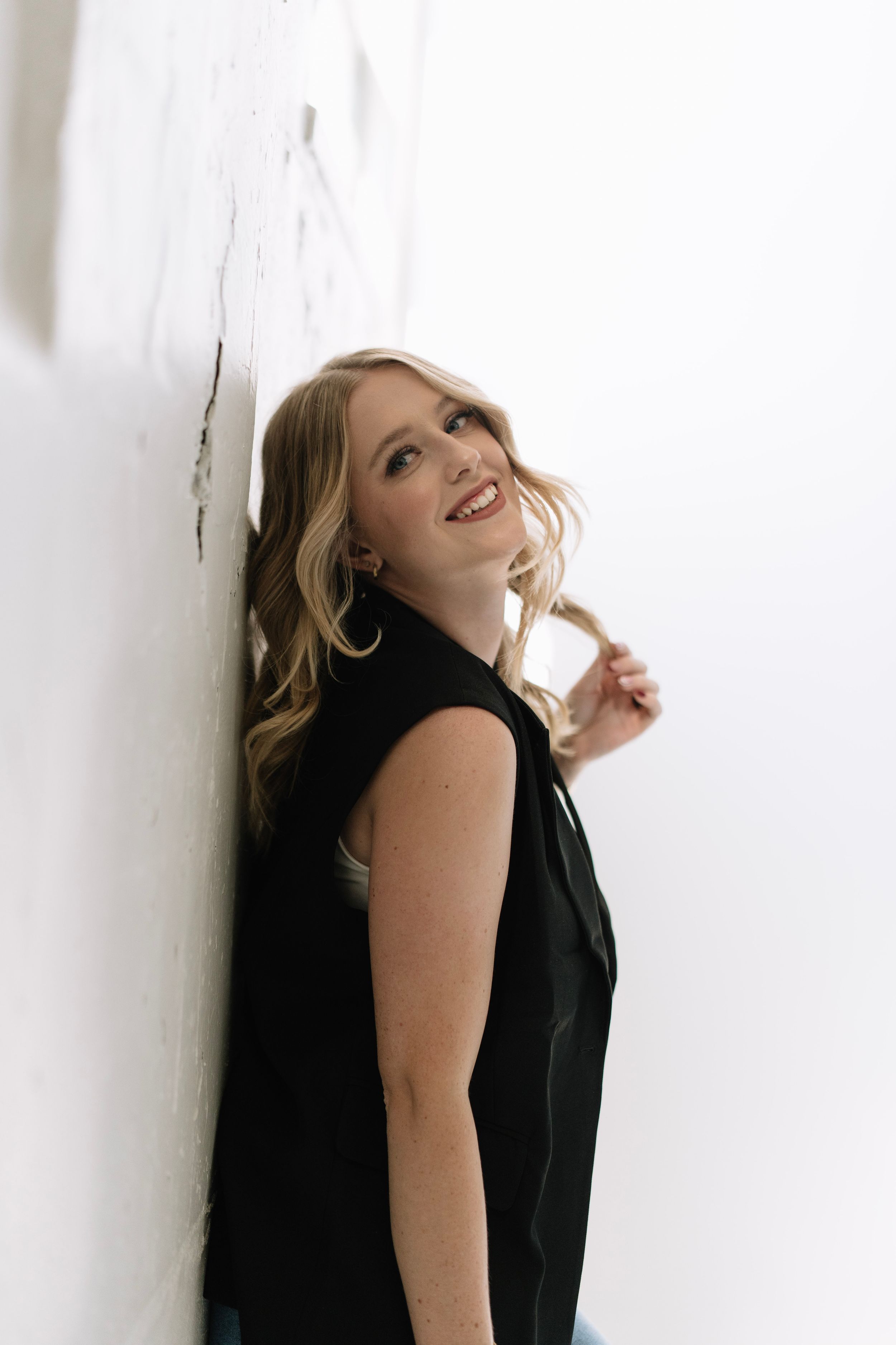 Woman in black blazer and dress smiles joyfully against white background.