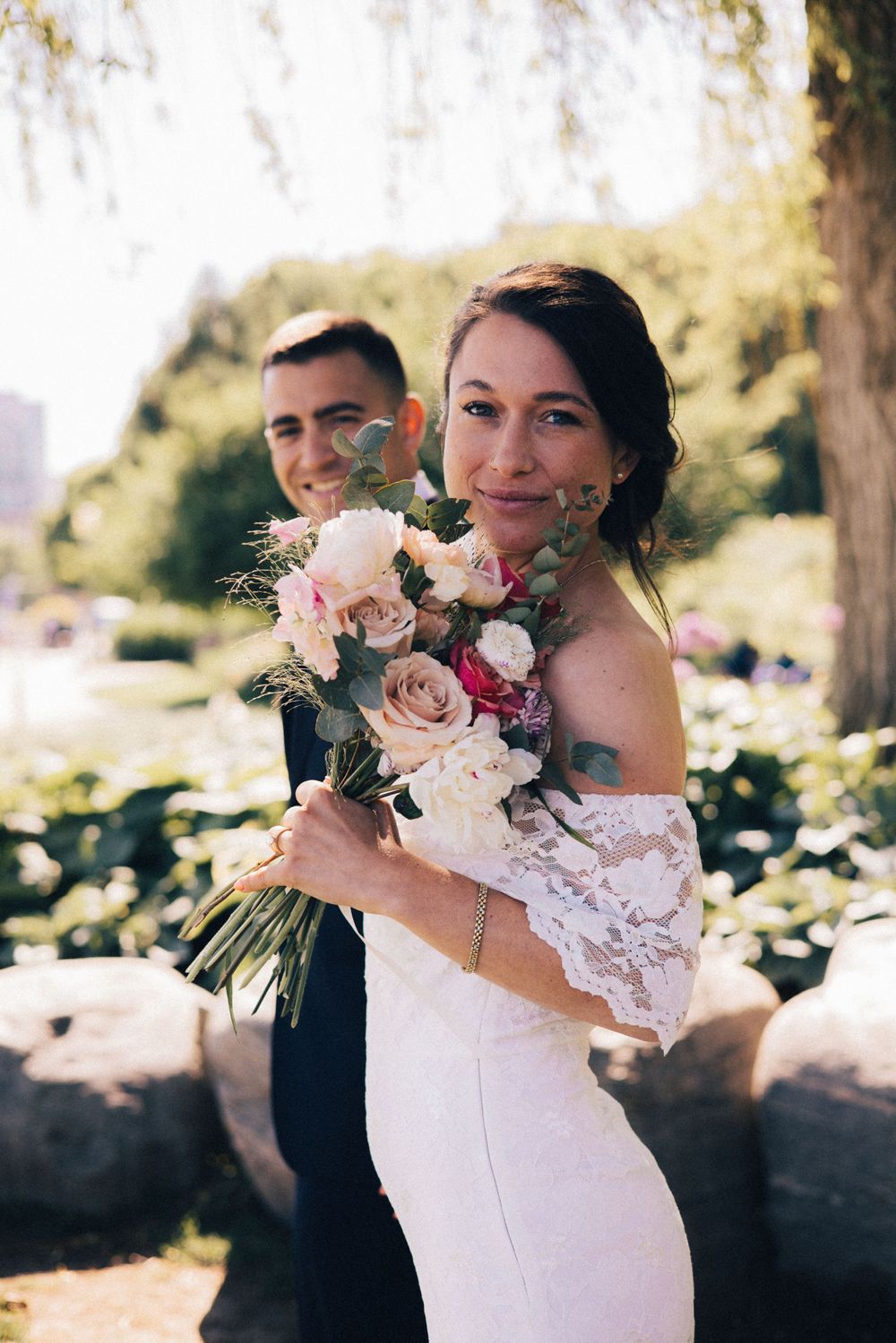 beautiful shot of bride holding a bouquet of flowers with the groom in the background in music garden at golden hour