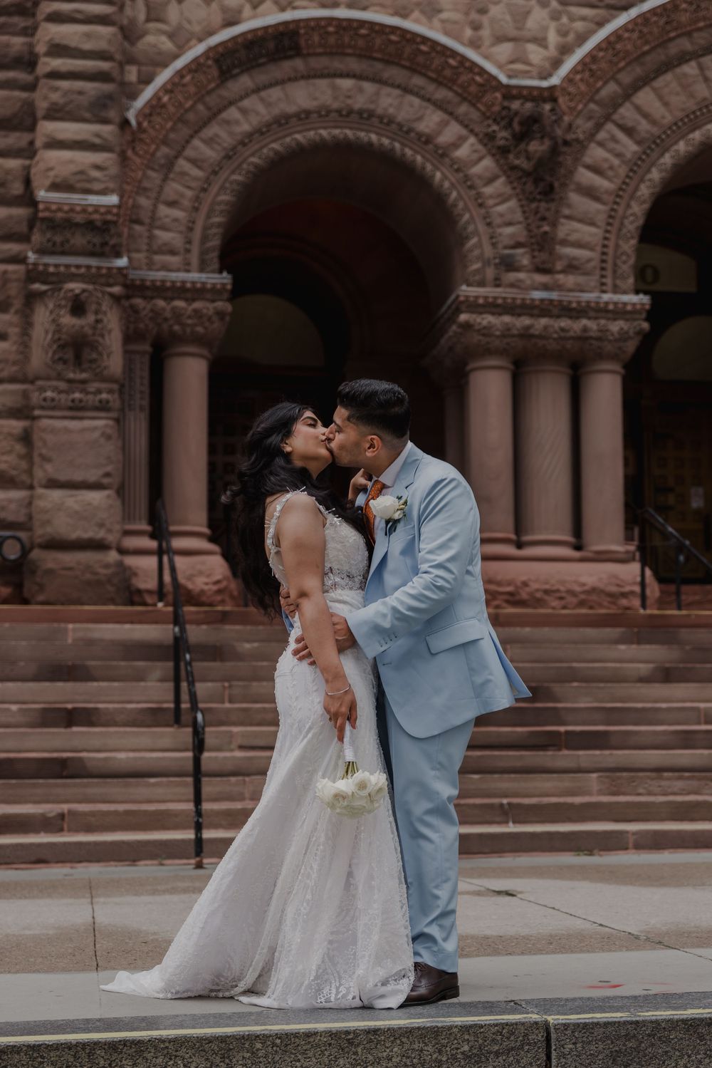 bride and groom sharing a kiss in front of a castle in toronto with beautiful light and clothing