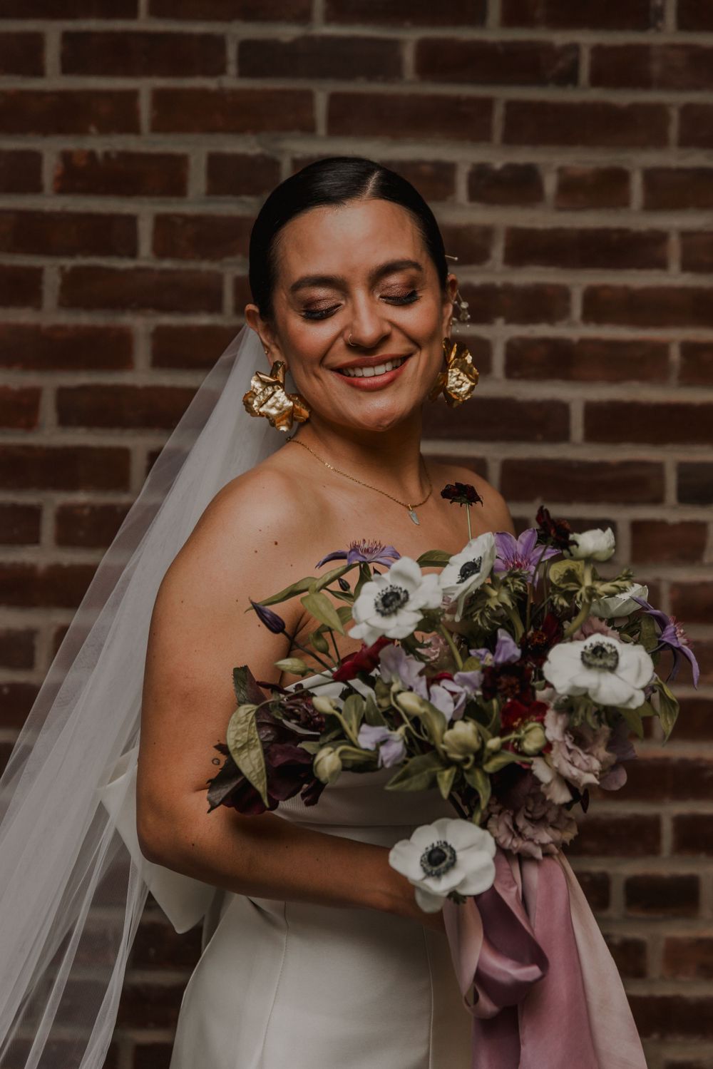 beautiful shot of bride with a brick backdrop holding a bouquet of flowers